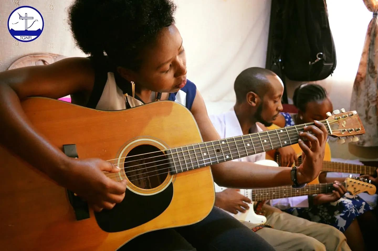 A guitarist leading worship practice, other players seated around her with guitars